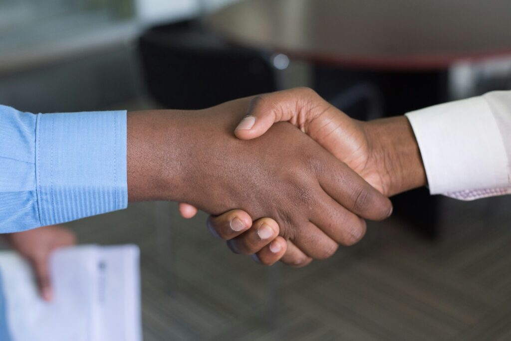 A close-up of a handshake-with-a-sold-sign-or-house-in-the-background